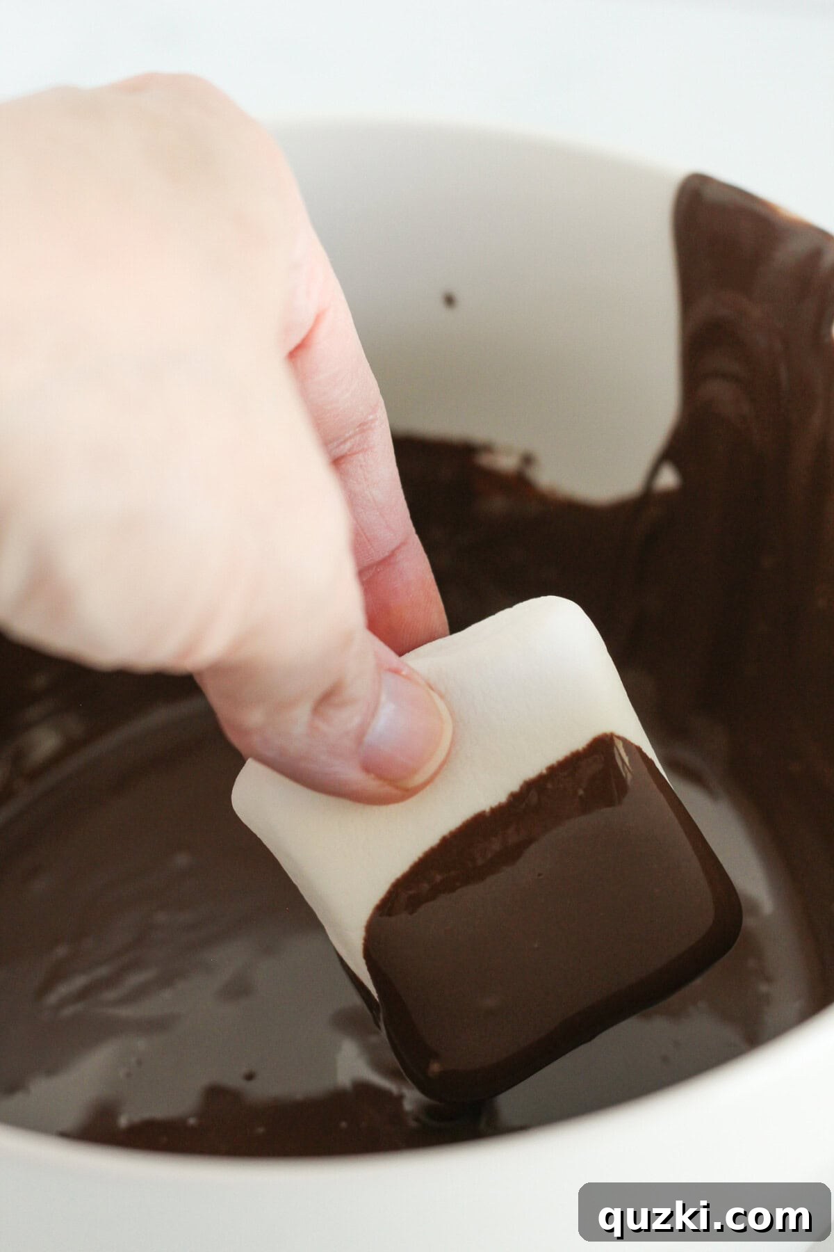 Easy Two-Ingredient Chocolate Dipped Marshmallows 5 A large marshmallow being carefully dipped into a bowl of smooth, melted chocolate.