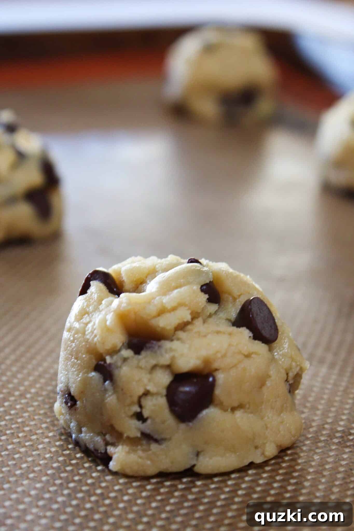 Melt-in-Your-Mouth Soft Chocolate Chip Delights 12 Large mounds of chocolate chip cookie dough scooped onto a baking sheet lined with silicone mat.