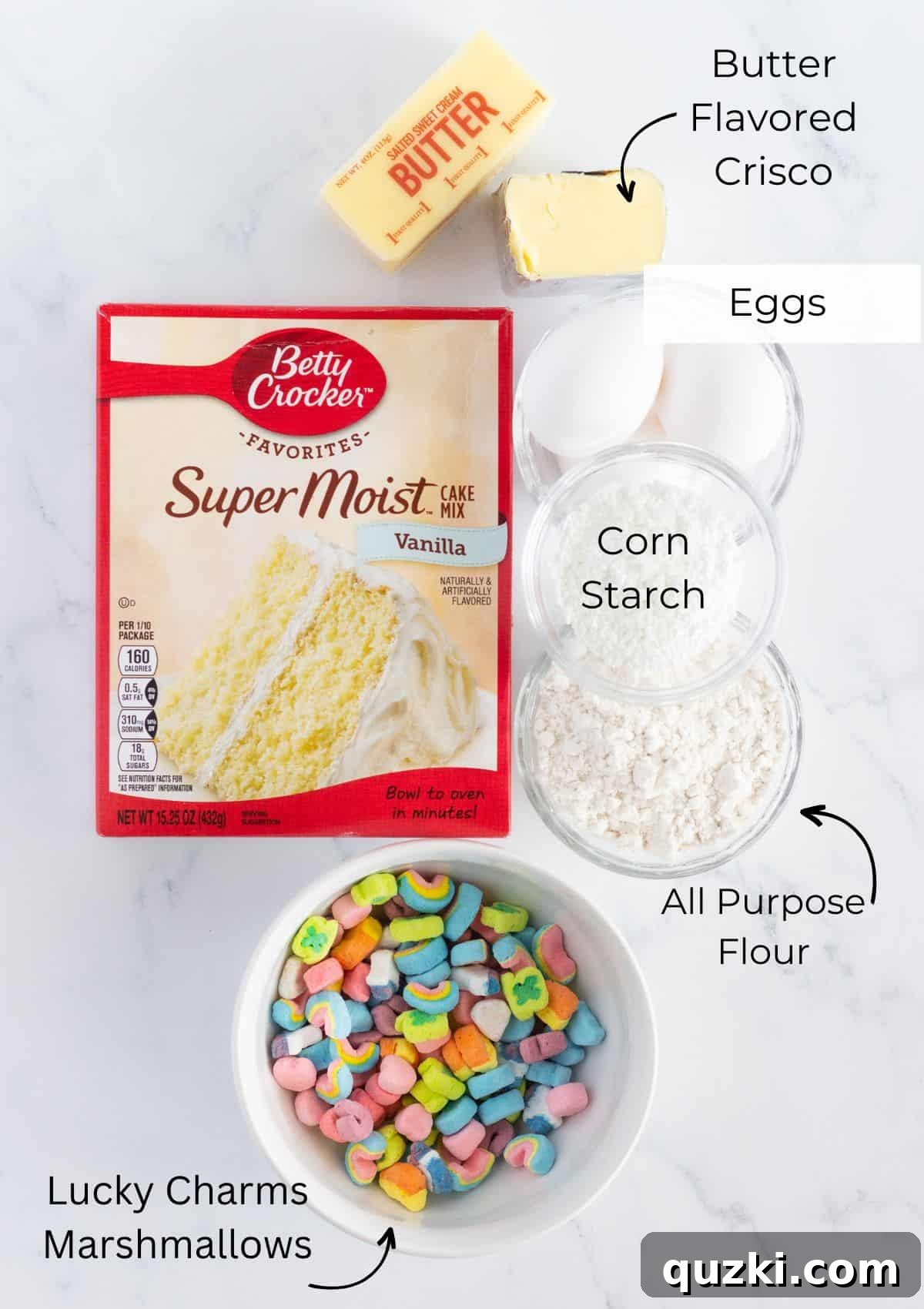 The essential ingredients needed to bake the Lucky Charms Cookies, including cake mix, cornstarch, flour, butter, Crisco, eggs, and Lucky Charms marshmallows, laid out on a clean surface.