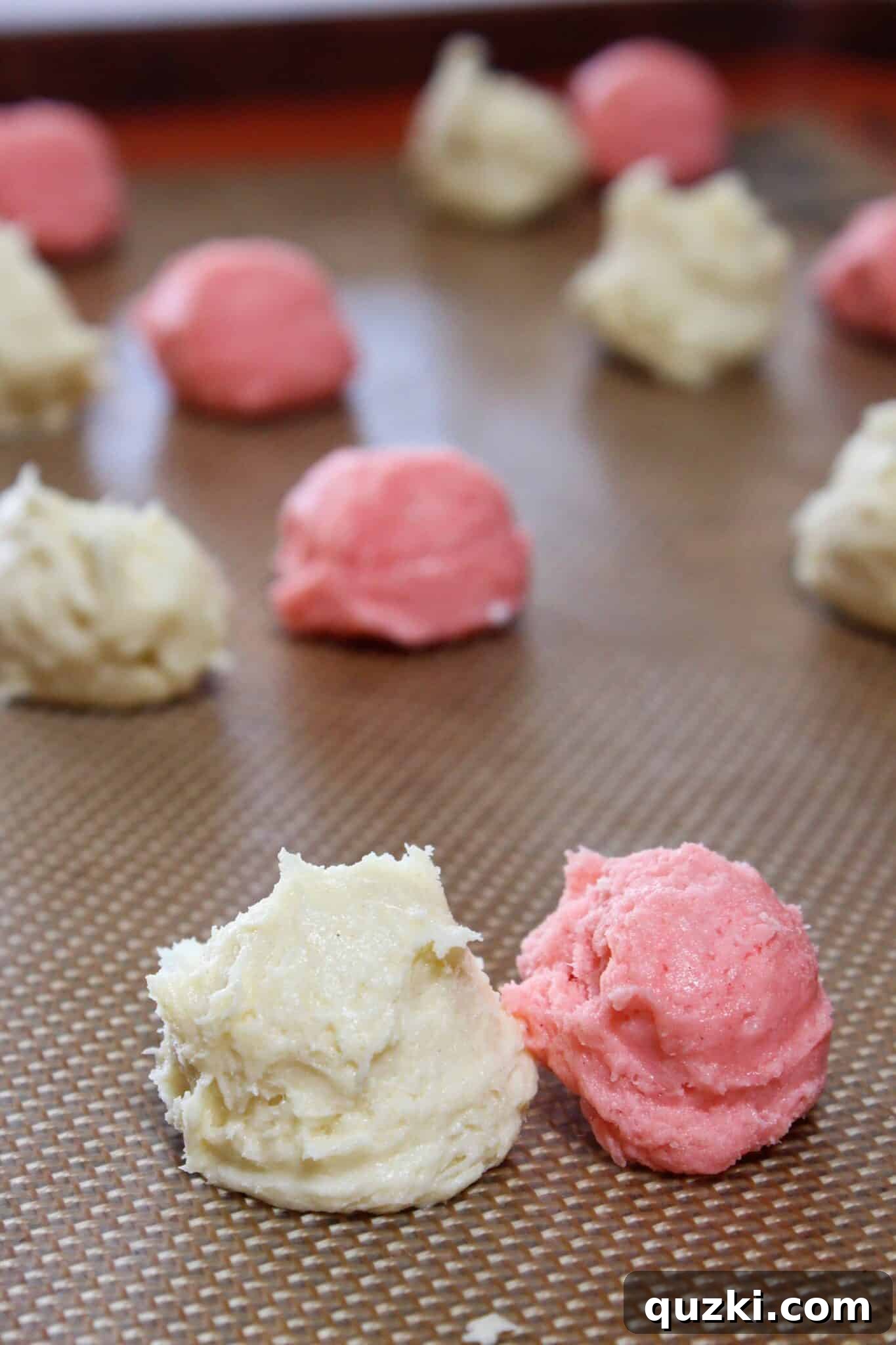 Separate mounds of vanilla and strawberry cookie dough on a surface, prepped for rolling