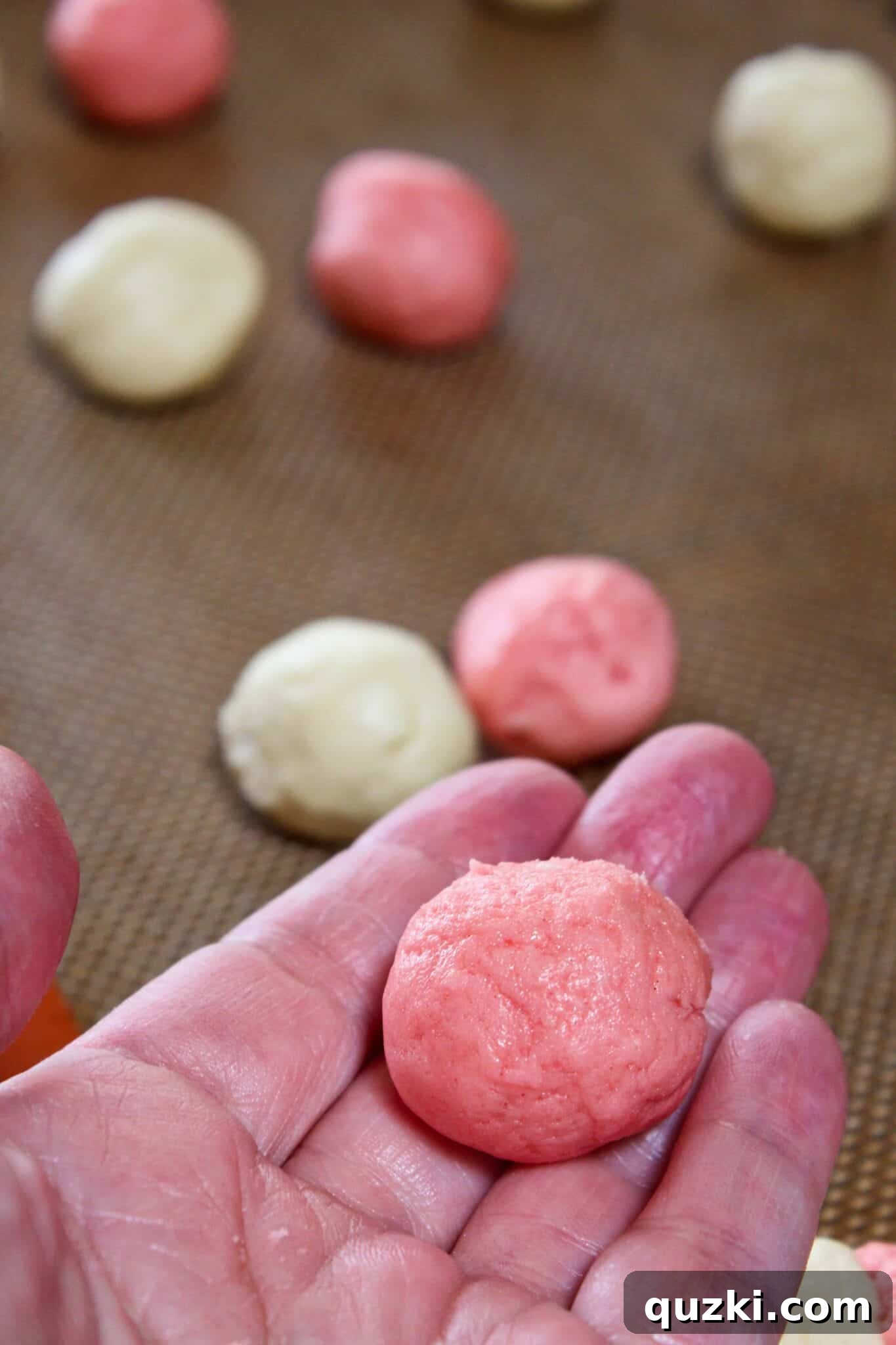 Hand rolling a scoop of cookie dough into a smooth round ball for consistent baking