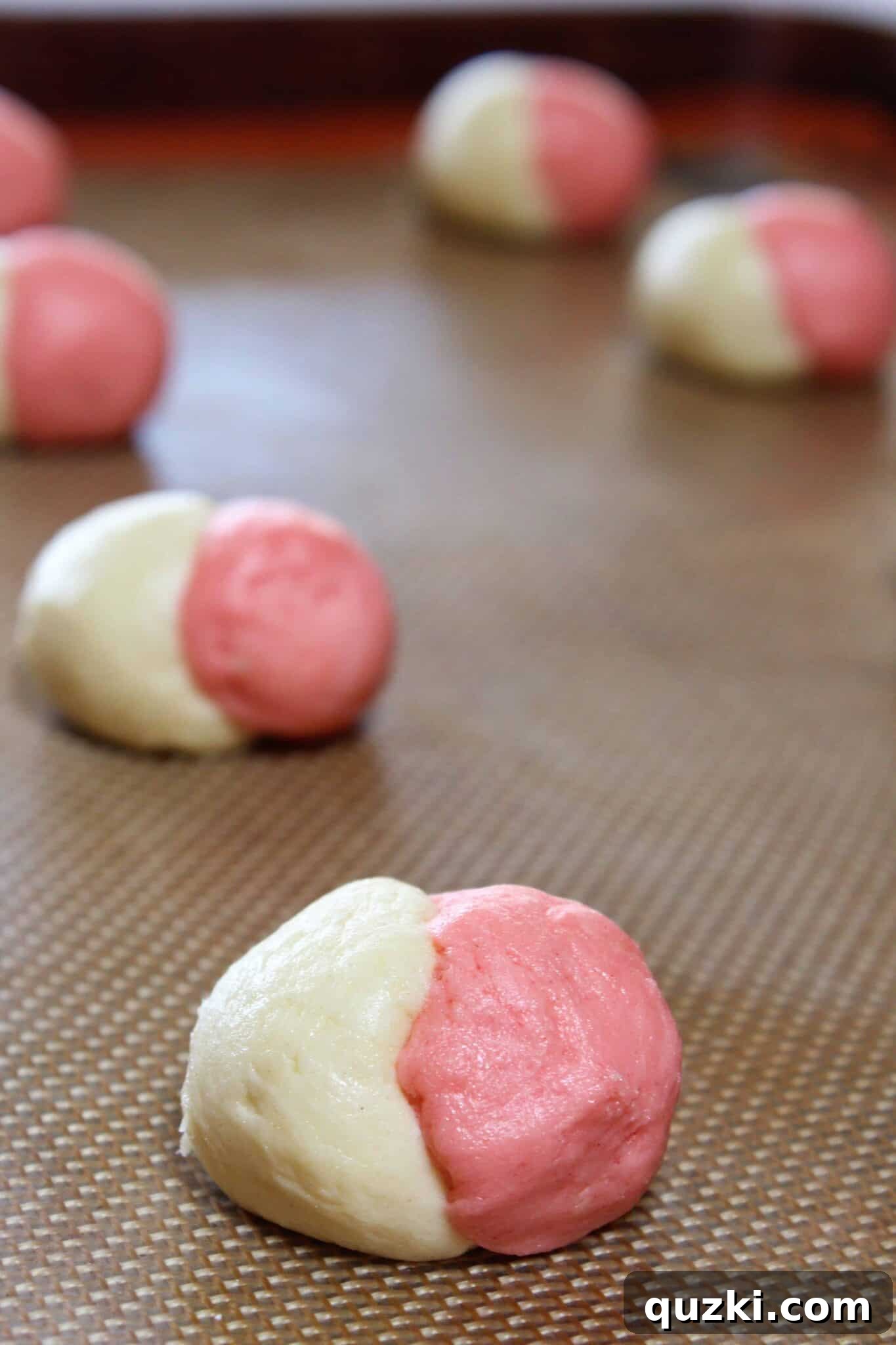 Vanilla and strawberry cookie dough balls rolled together, forming a perfect Neapolitan swirl before baking