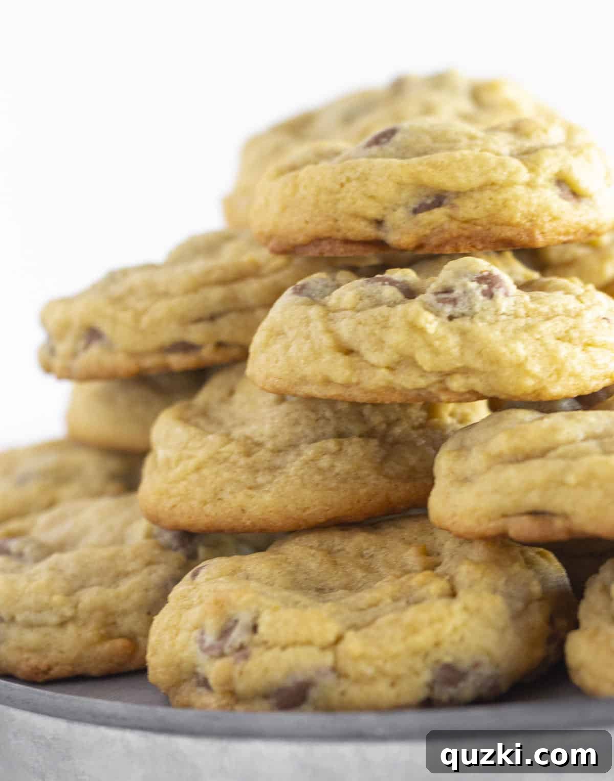 Stacks of soft chocolate chip cookies generously piled onto a galvanized metal plate, inviting you to take a bite.