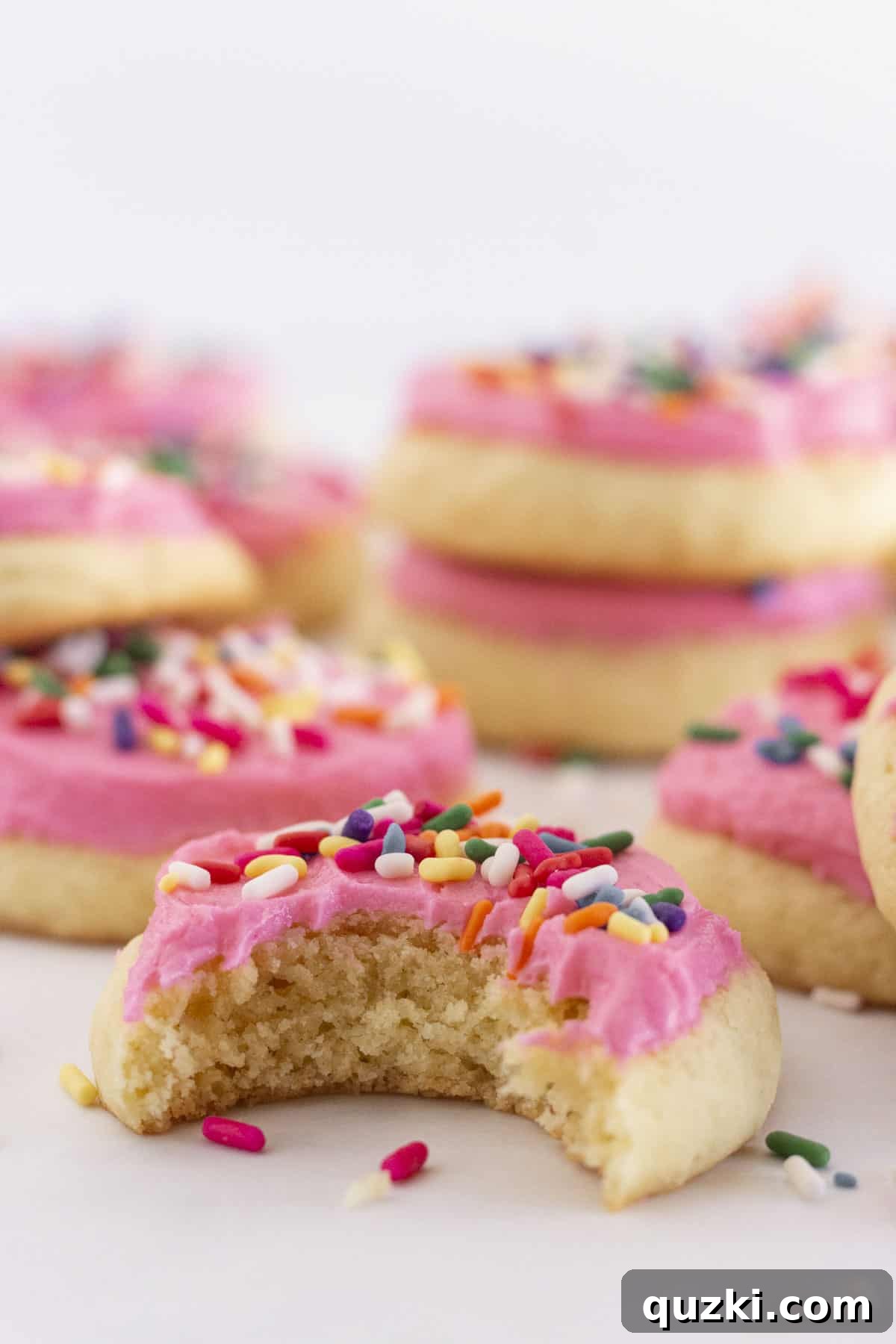 Cloudlike Lofthouse Sugar Cookies 6 A selection of frosted Lofthouse sugar cookies artfully arranged on a tray, with one cookie showing a bite taken out of it to reveal its soft interior.