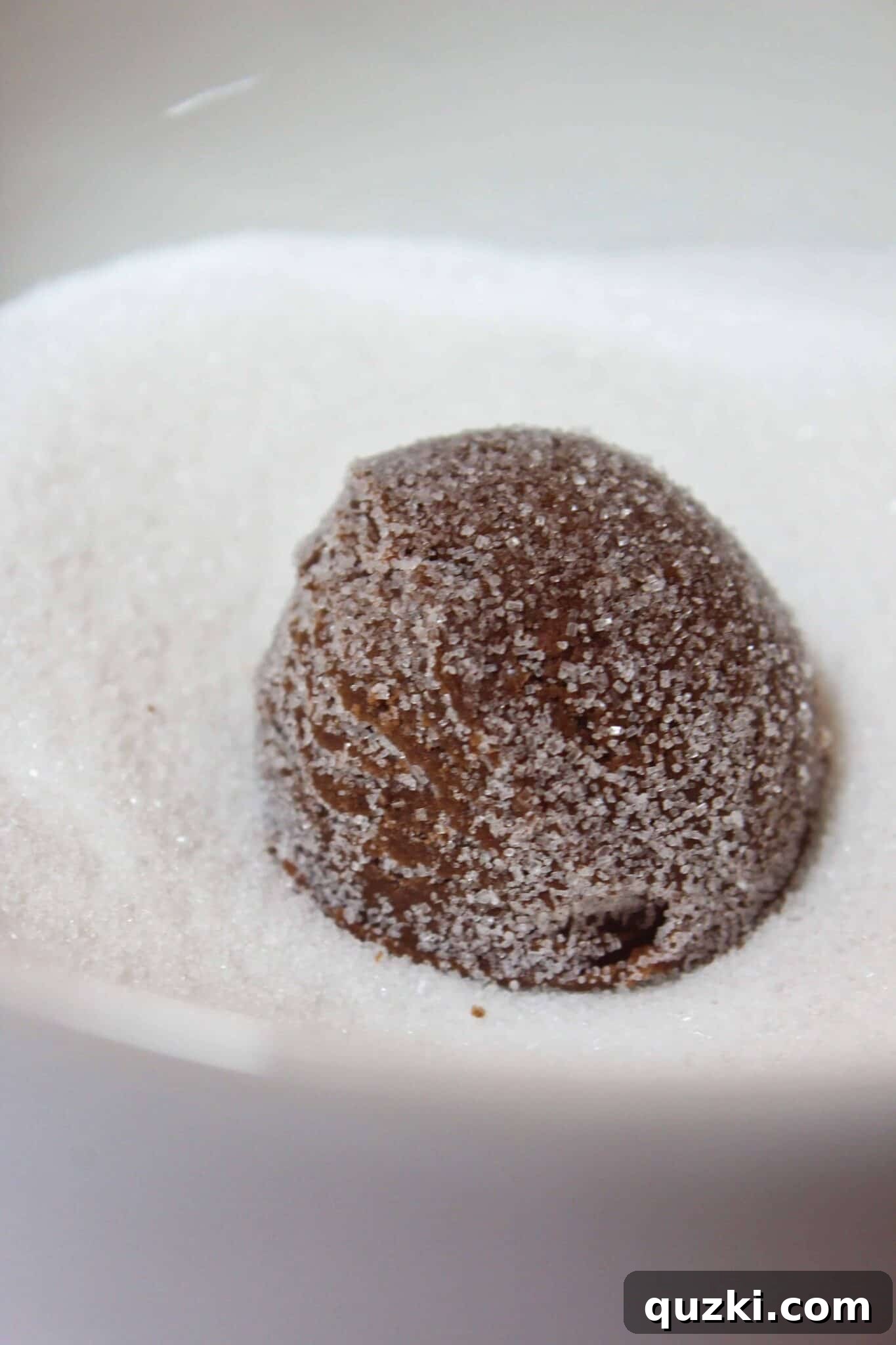 Cookie dough balls being scooped and then meticulously rolled in granulated sugar before baking.