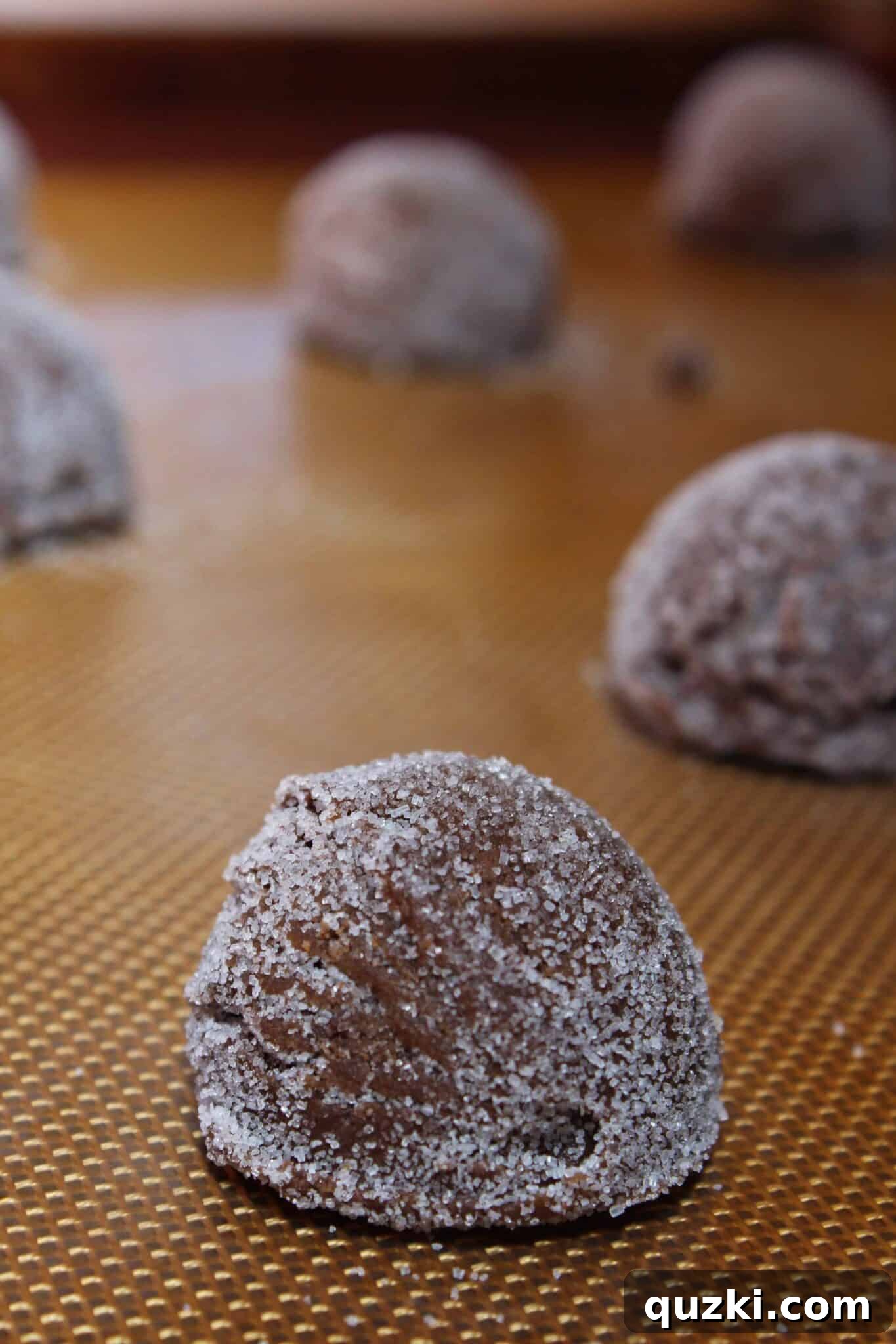 The signature fork crisscross pattern being pressed into the top of chocolate peanut butter cookie dough balls on a baking sheet.