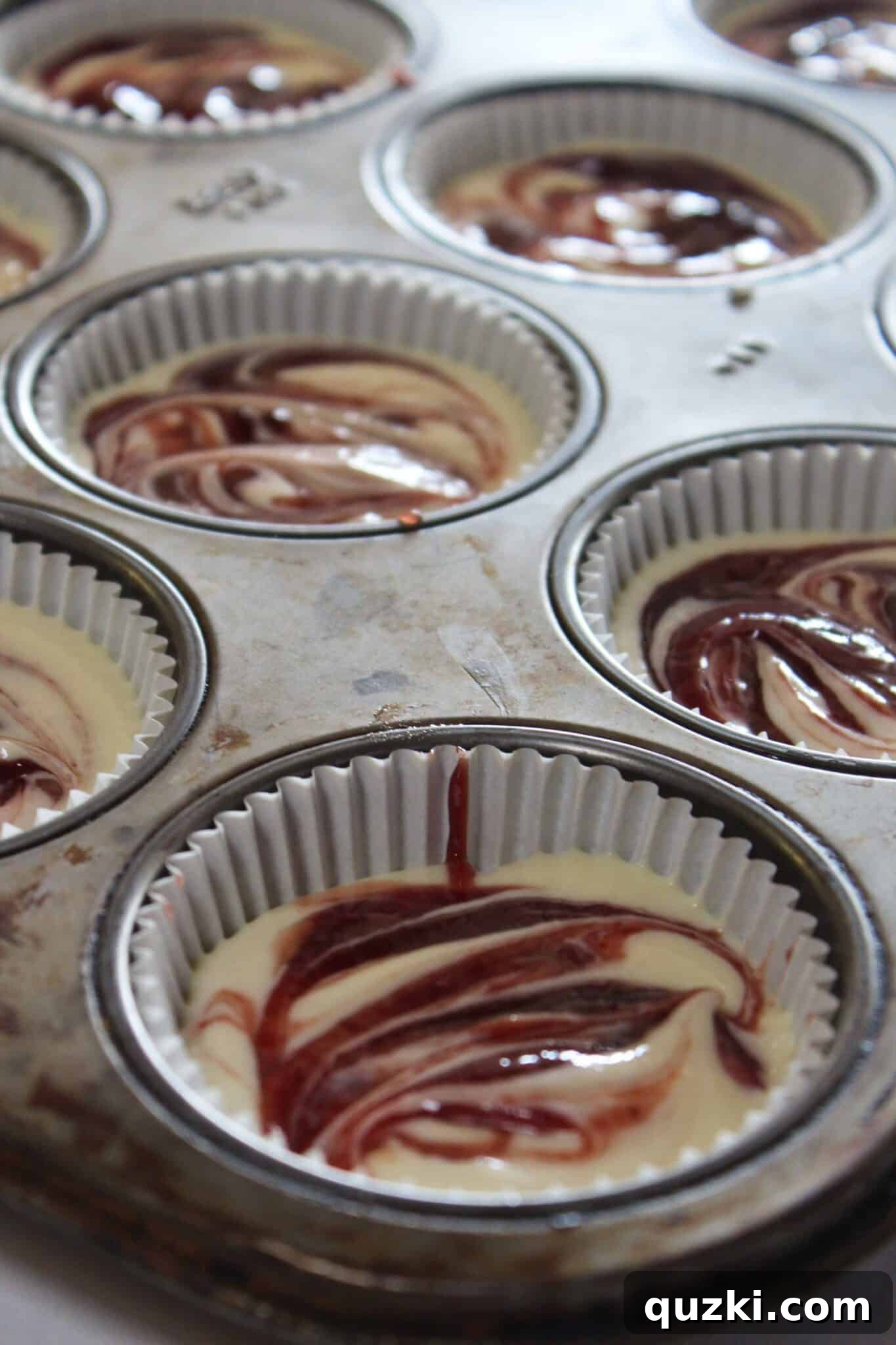 Decadent Mini Raspberry Cheesecake Cups 12 Beautifully swirled Mini Raspberry Cheesecakes in a muffin tin, ready for chilling.