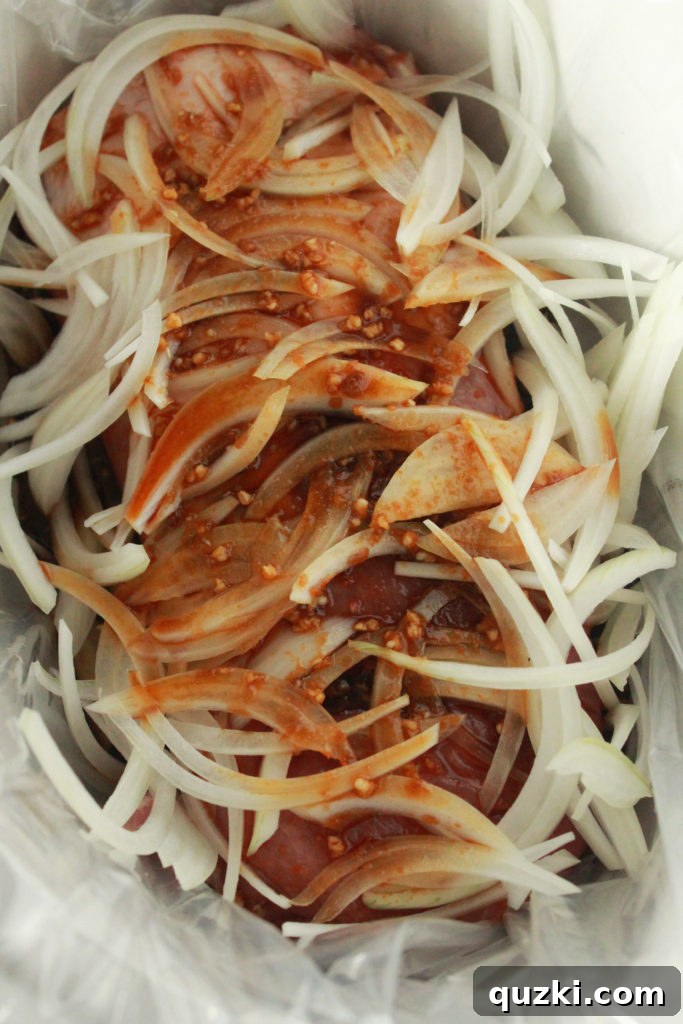 Pork roast and sliced onions placed in a crock pot with a liner, ready for the Korean marinade to be poured over.