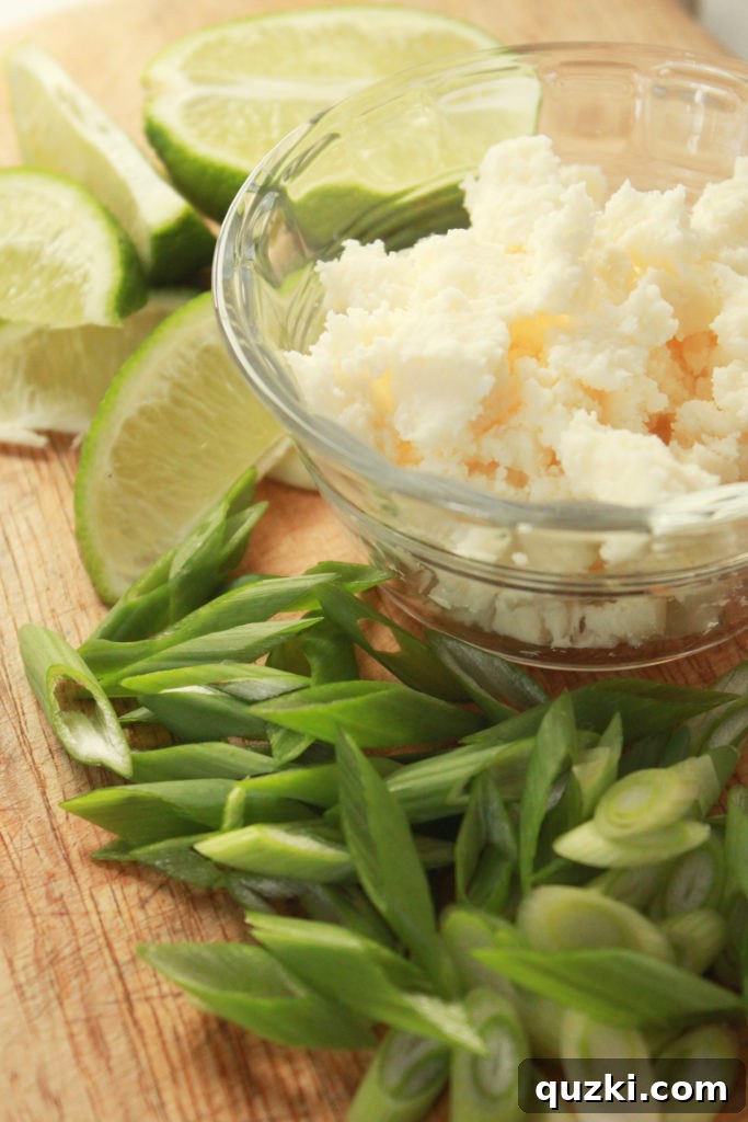 An array of fresh taco toppings including lime wedges, sliced green onions, and crumbled queso fresco cheese.