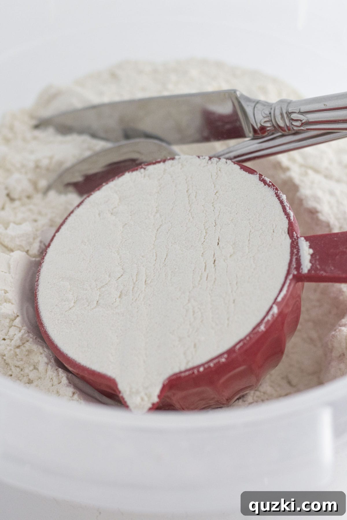 Demonstrating the 'spoon and level' method for accurately measuring flour using a spoon and a knife to level it off.