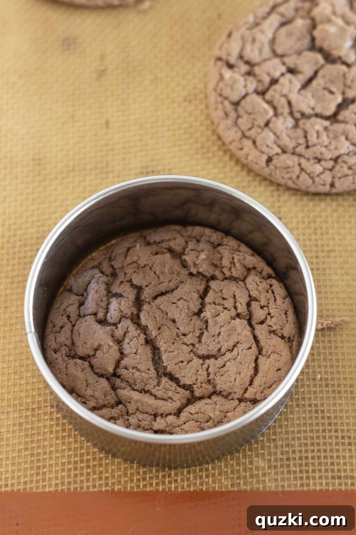 Using a larger round cookie cutter to gently shape a warm, freshly baked cookie into a perfect circle.