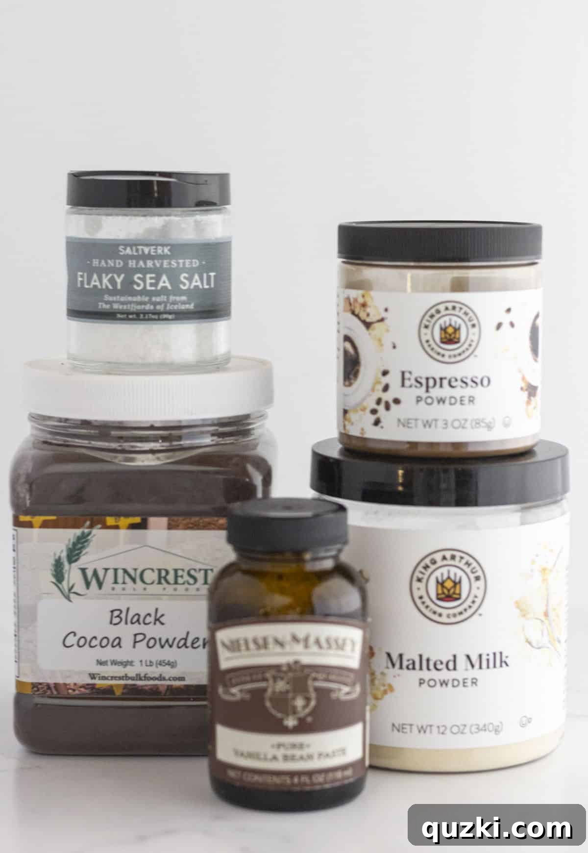 A selection of high-end and specialty baking ingredients like vanilla bean paste, flaky sea salt, black cocoa, and espresso powder.