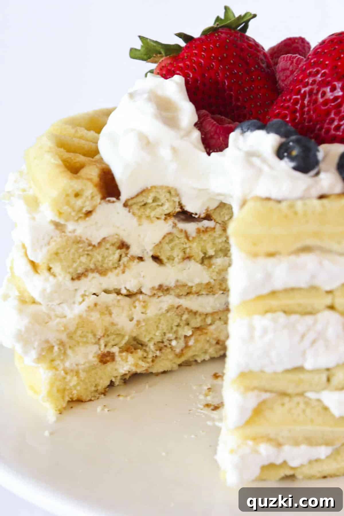 Towering Vanilla Waffle Cake 6 A slice perfectly removed from a layered vanilla waffle cake, showcasing the beautiful layers of waffle cake, whipped cream, and fresh berries.