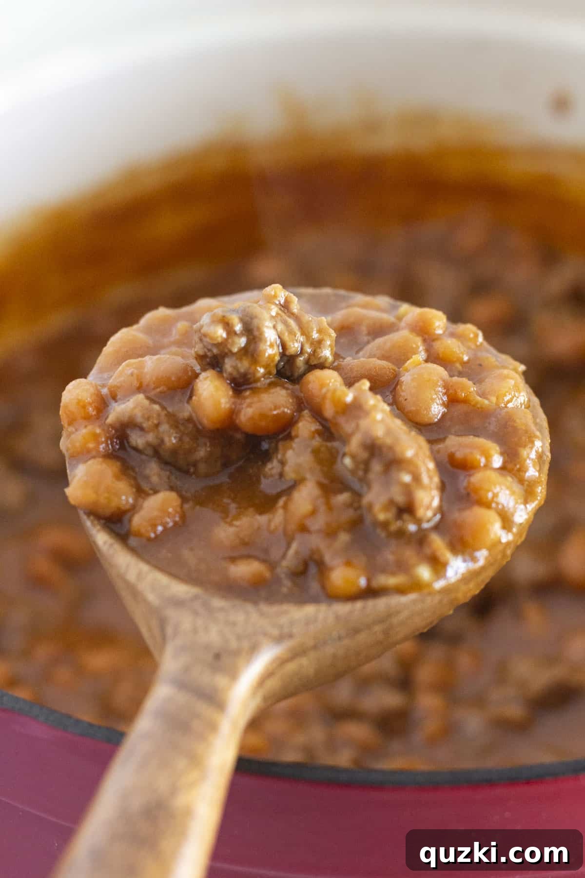 Hearty Ground Beef Baked Beans 2 A serving spoon lifting a portion of hearty baked beans with ground beef from a rustic dish, showcasing the rich texture and vibrant sauce.