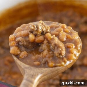 Serving a spoon of baked beans with ground beef, highlighting the rich texture and hearty ingredients.