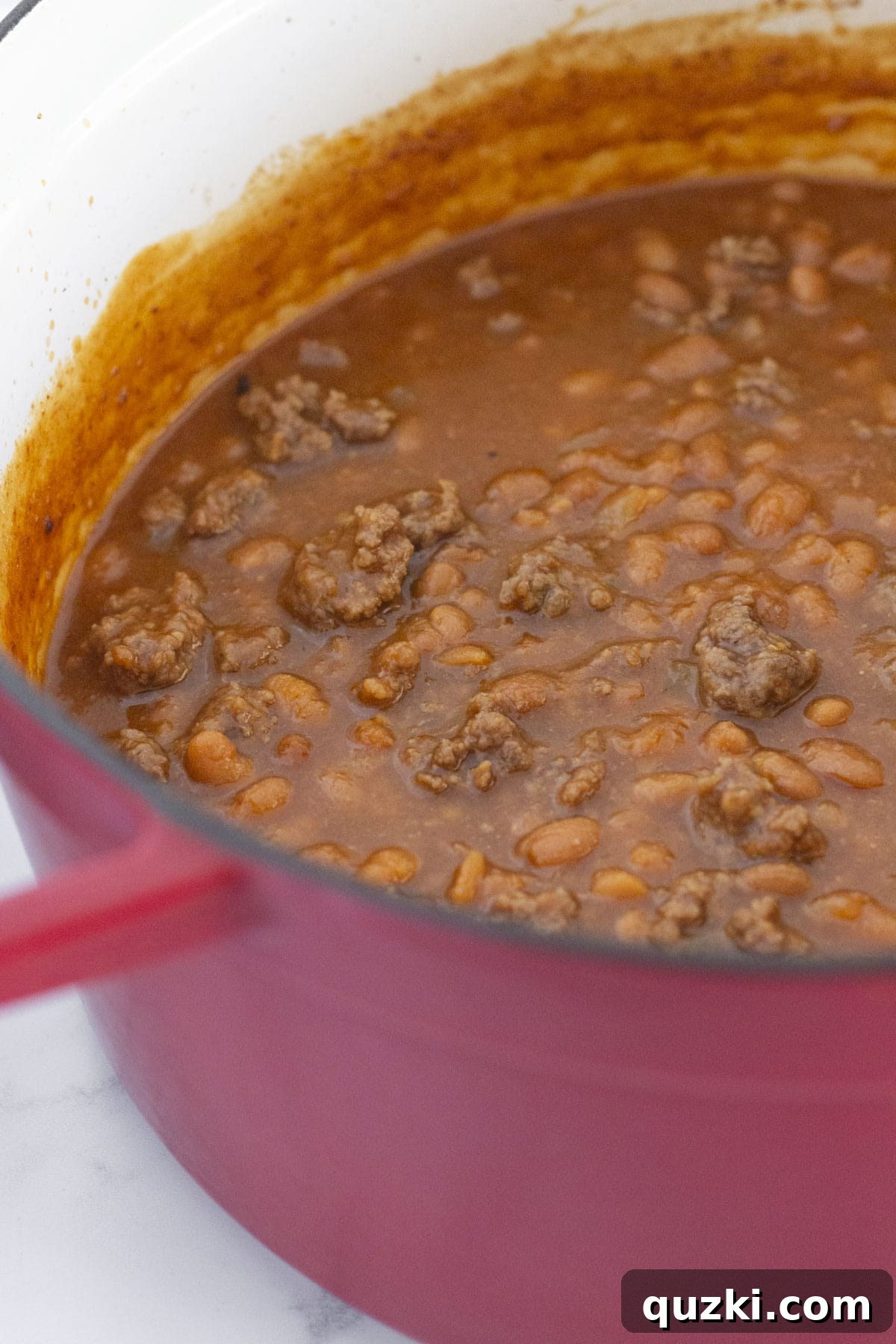 Hearty Ground Beef Baked Beans 6 A close-up view looking down into a large pot filled with steaming baked beans with ground beef, showing the rich, thick sauce and visible chunks of meat and beans.