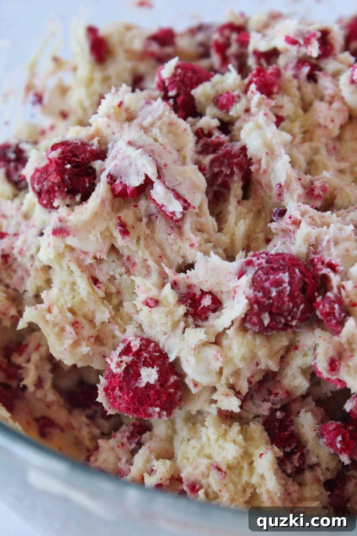 Subway's Iconic Raspberry Cheesecake Cookies Make Them At Home 7 Close up of cookie dough with white chocolate chips and freeze-dried raspberries evenly combined, showing slight breakage of raspberries.