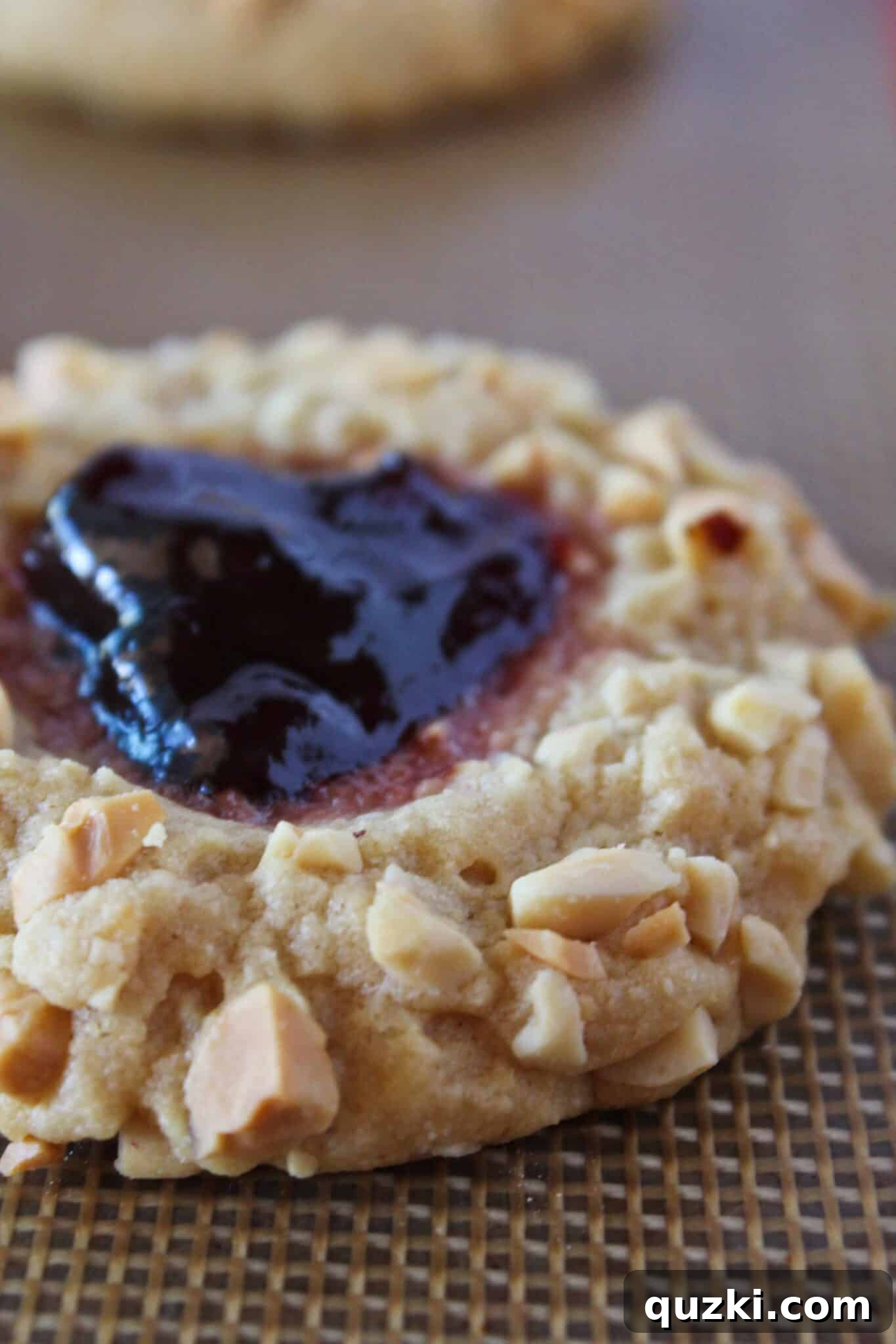 Baked PB&J Cookies with jam centers cooling on a cookie sheet.