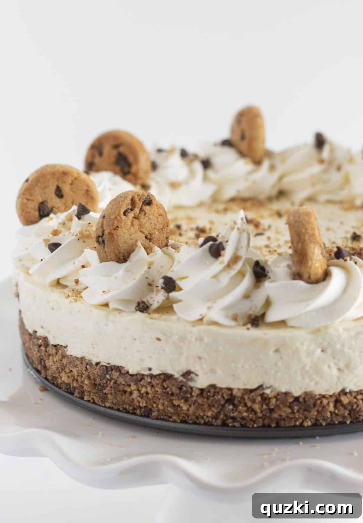 A beautifully plated finished chocolate chip cookie cheesecake, garnished with a swirl of whipped topping and mini chocolate chip cookies.