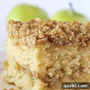 A square of apple crumb cake with a couple fresh apples in the background.