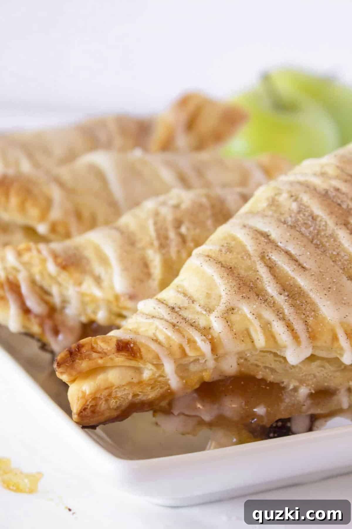 Sweet & Simple Caramel Apple Turnovers 10 A beautifully glazed Caramel Apple Turnover resting on a pristine white plate, garnished with a light dusting of cinnamon sugar, perfect for breakfast or dessert.