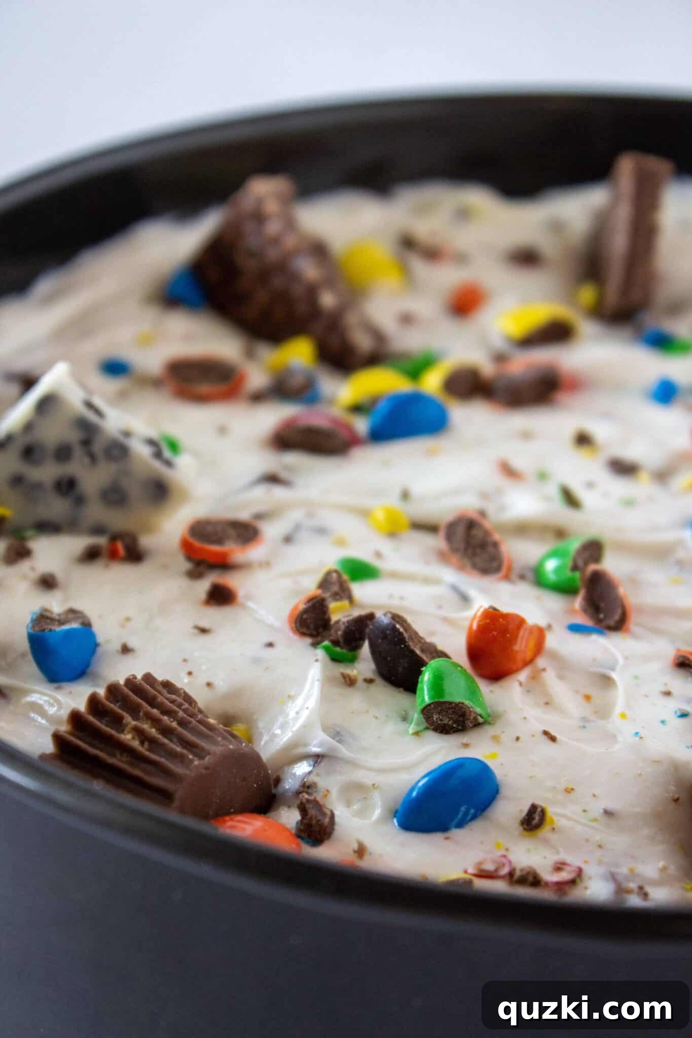 Frightfully Delicious No-Bake Candy Cheesecake 11 A top-down view of the cheesecake filling being added to the crust and decorated with extra Halloween candy.