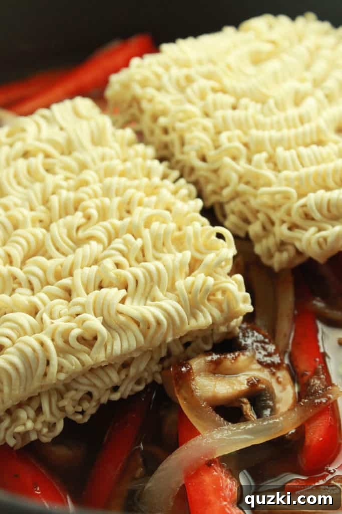 Hearty Skillet Beef Ramen 7 Ramen noodles and seasoning packets being added to the skillet with cooked vegetables and sauce