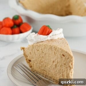 A slice of creamy pumpkin mousse pie, topped with a dollop of whipped cream, on a simple white plate.