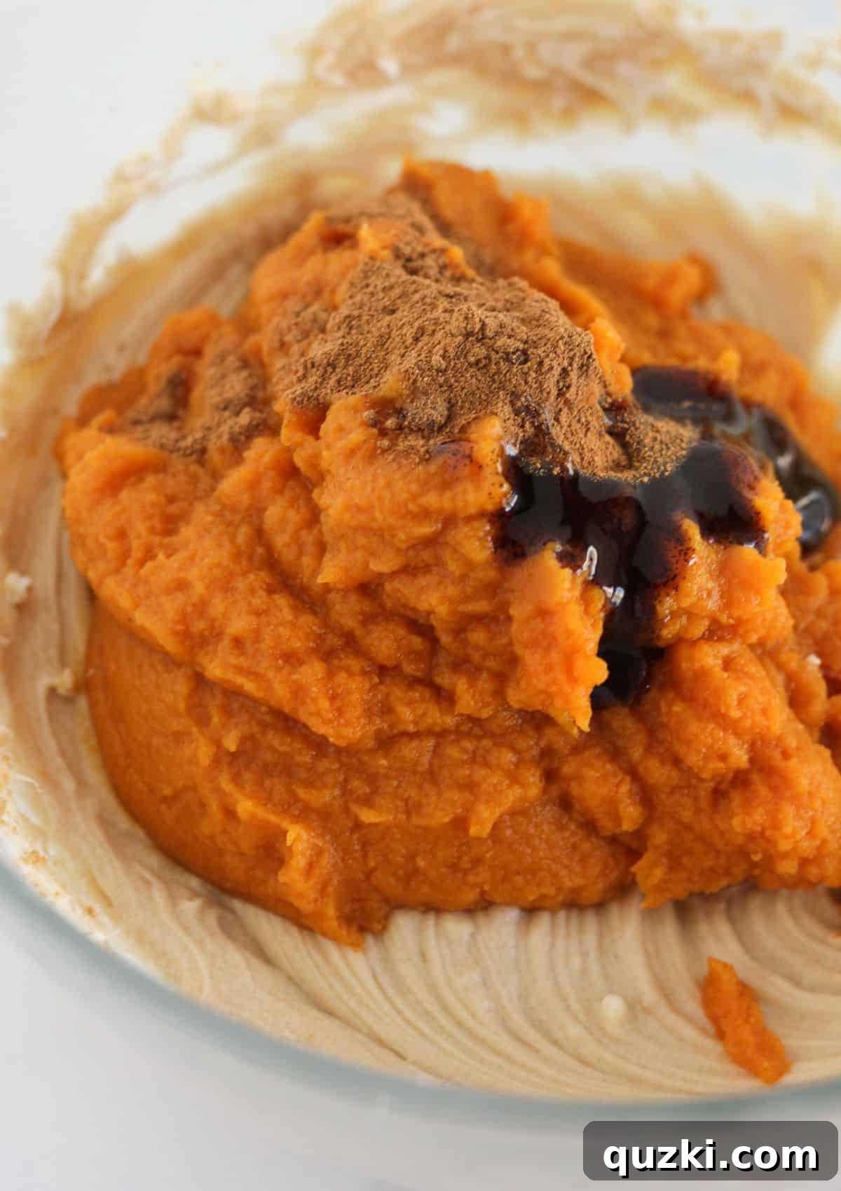Cream cheese and brown sugar are being beaten in a bowl with an electric mixer, before pumpkin puree and spices are added.