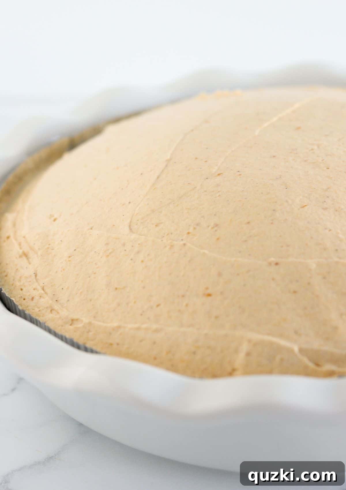 The creamy pumpkin mousse filling is being spooned and spread evenly into a pre-made graham cracker pie crust.