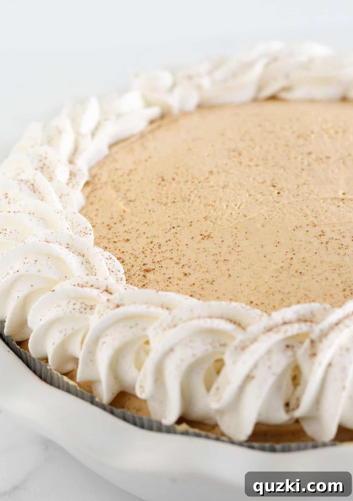 A chilled pumpkin mousse pie is being garnished with additional swirls of whipped topping, ready for serving.