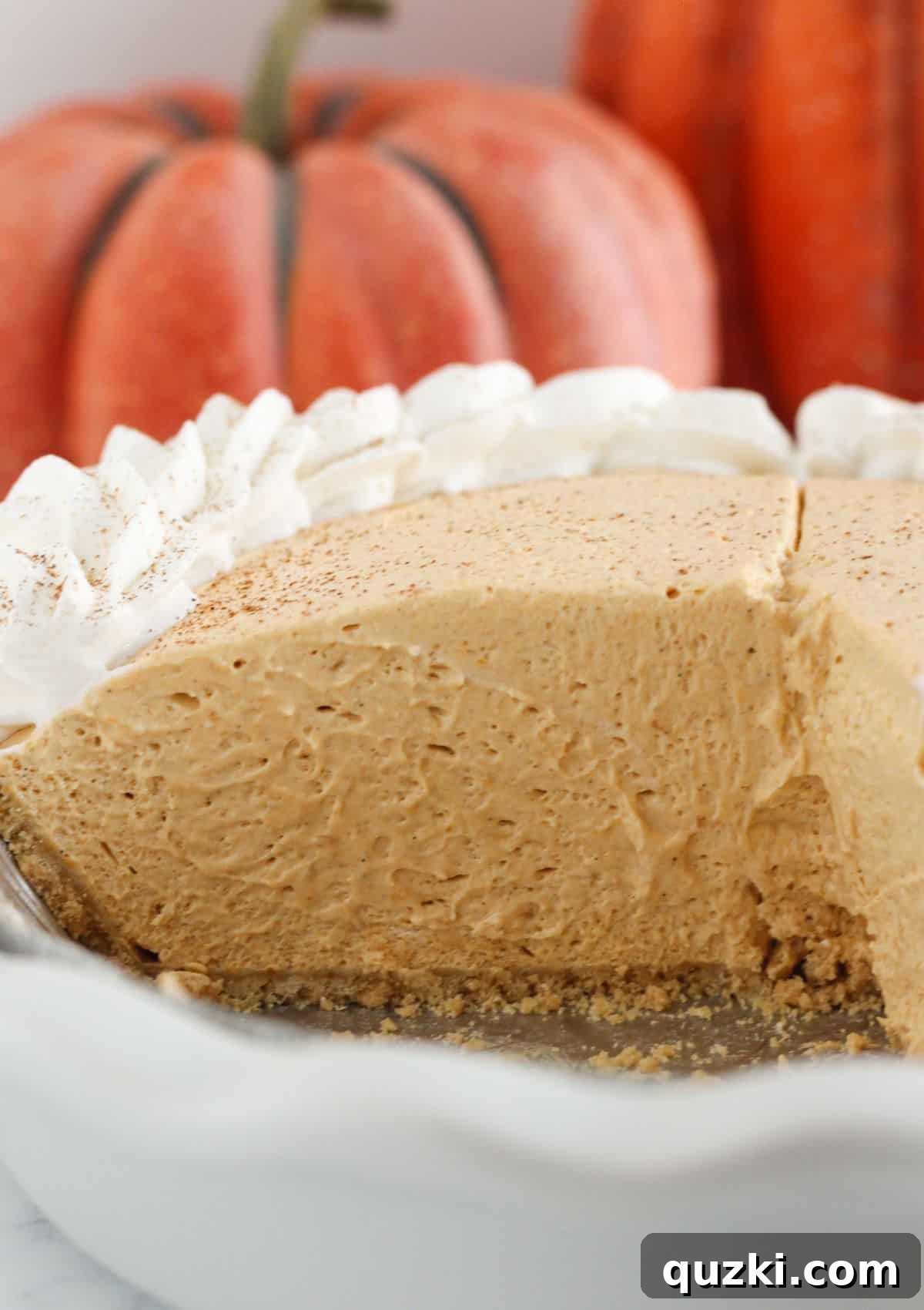 A pumpkin mousse pie with several slices already taken, revealing its creamy texture and graham cracker crust, garnished with whipped cream.