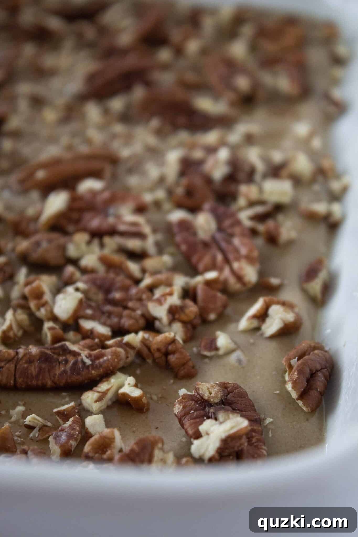 Caramel sauce with a mixture of whole and chopped pecans spread in a baking pan for sticky buns