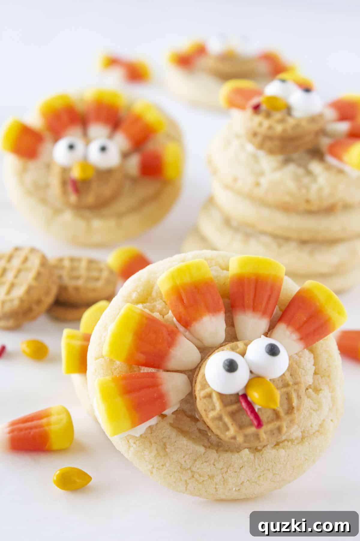 Effortless Thanksgiving Turkey Cookies 7 Stacked turkey cookies on a white plate, with a bowl of candy corn and edible eyes in the background, showing the ingredients used for decoration.