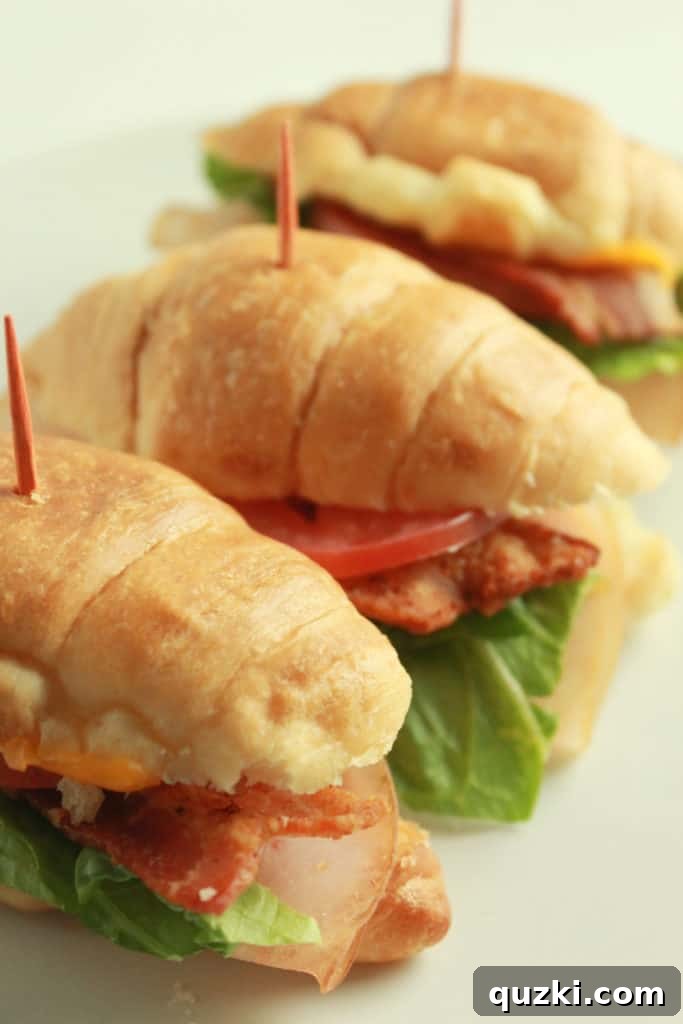 Elevated Croissant Club Sliders 6 A hand reaching for a Club Sandwich Croissant Slider, illustrating their grab-and-go appeal.