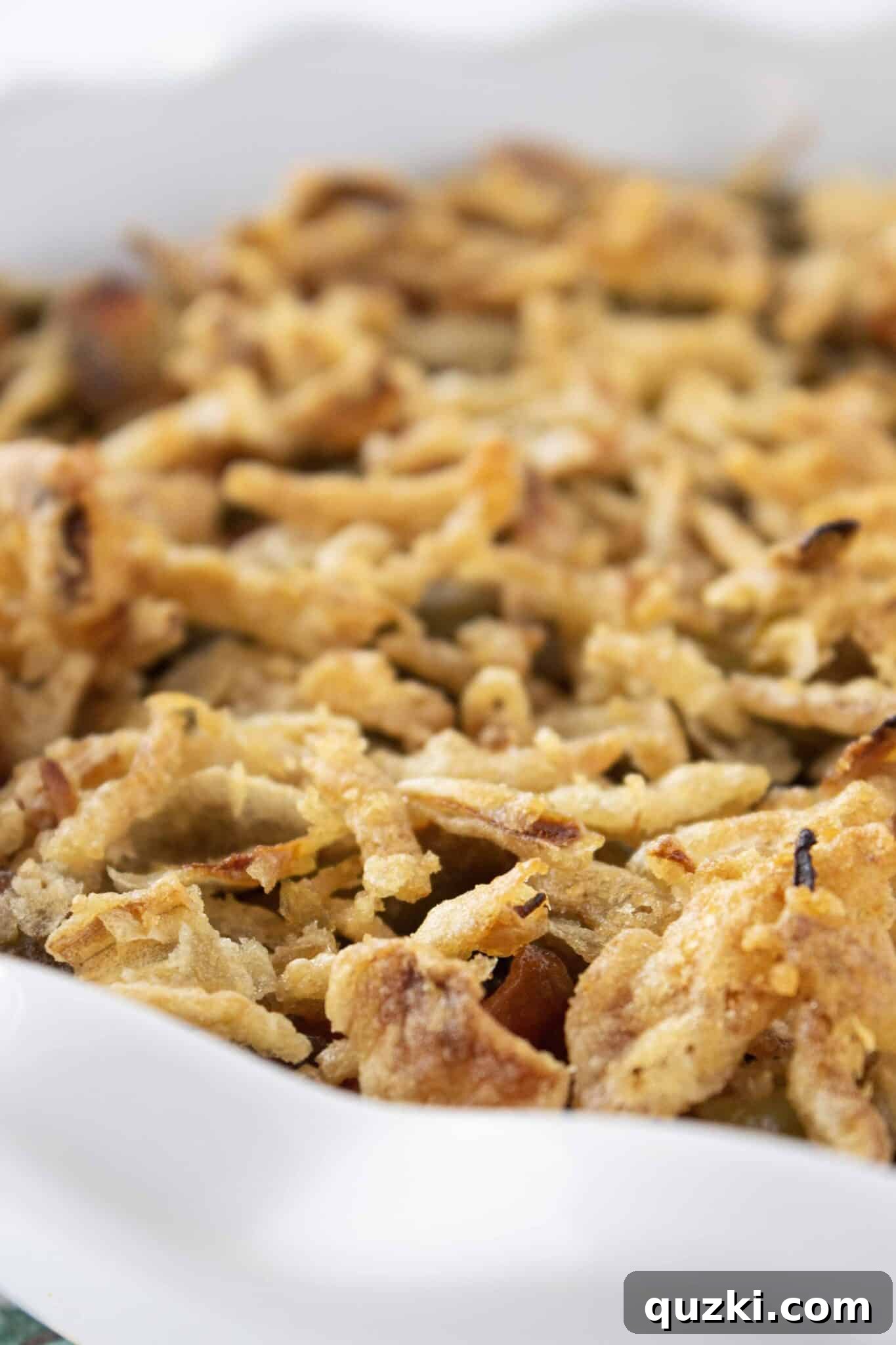 Carefully topping the assembled BBQ Green Bean Casserole with a generous layer of French fried onions before baking.