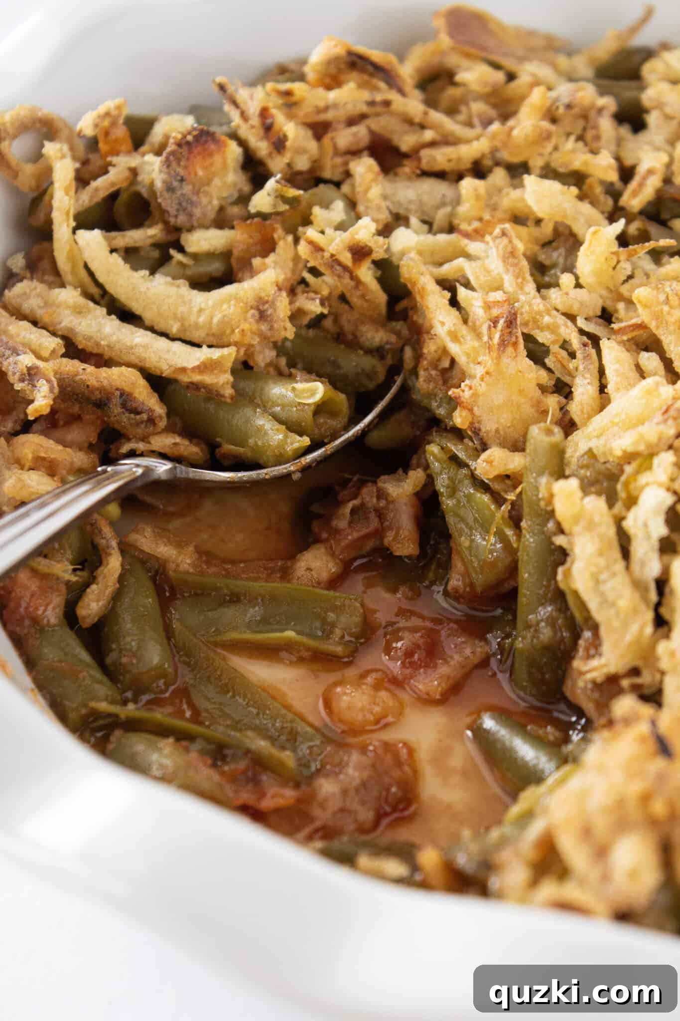 A close-up of the delicious BBQ Green Bean Casserole with a serving spoon, highlighting its texture and irresistible appeal.