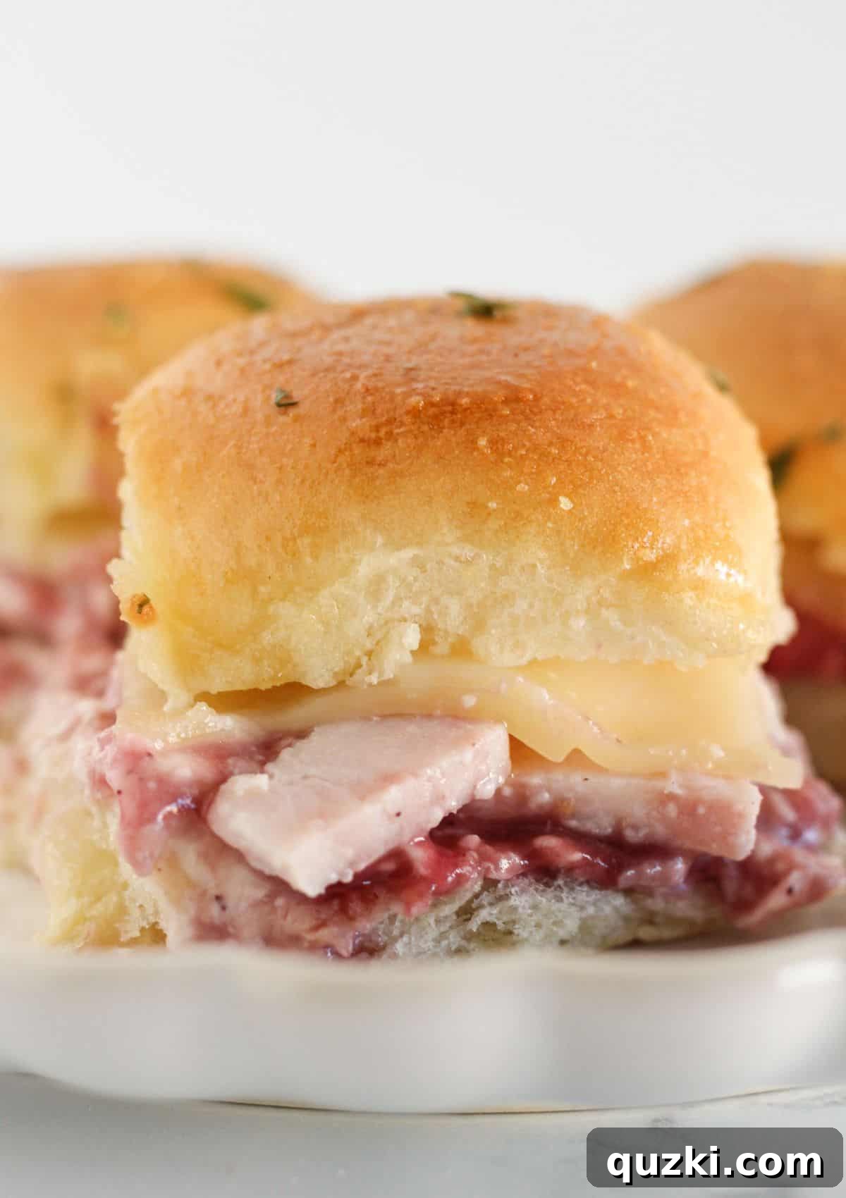 Three elegant Turkey Sliders with Cranberry Cream Cheese Spread on buttery croissants, served on a plate.