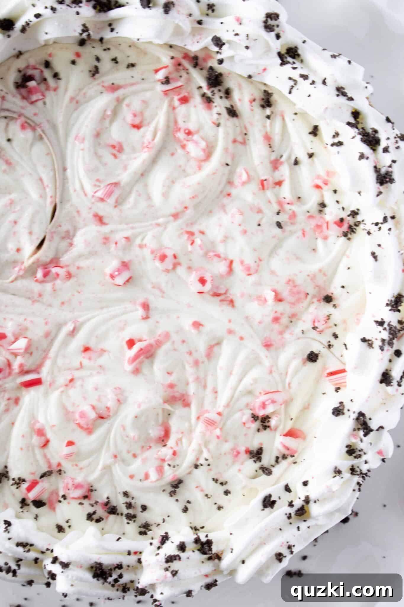 Decorating the edge of the cheesecake with whipped cream and crushed Oreo crumbs.