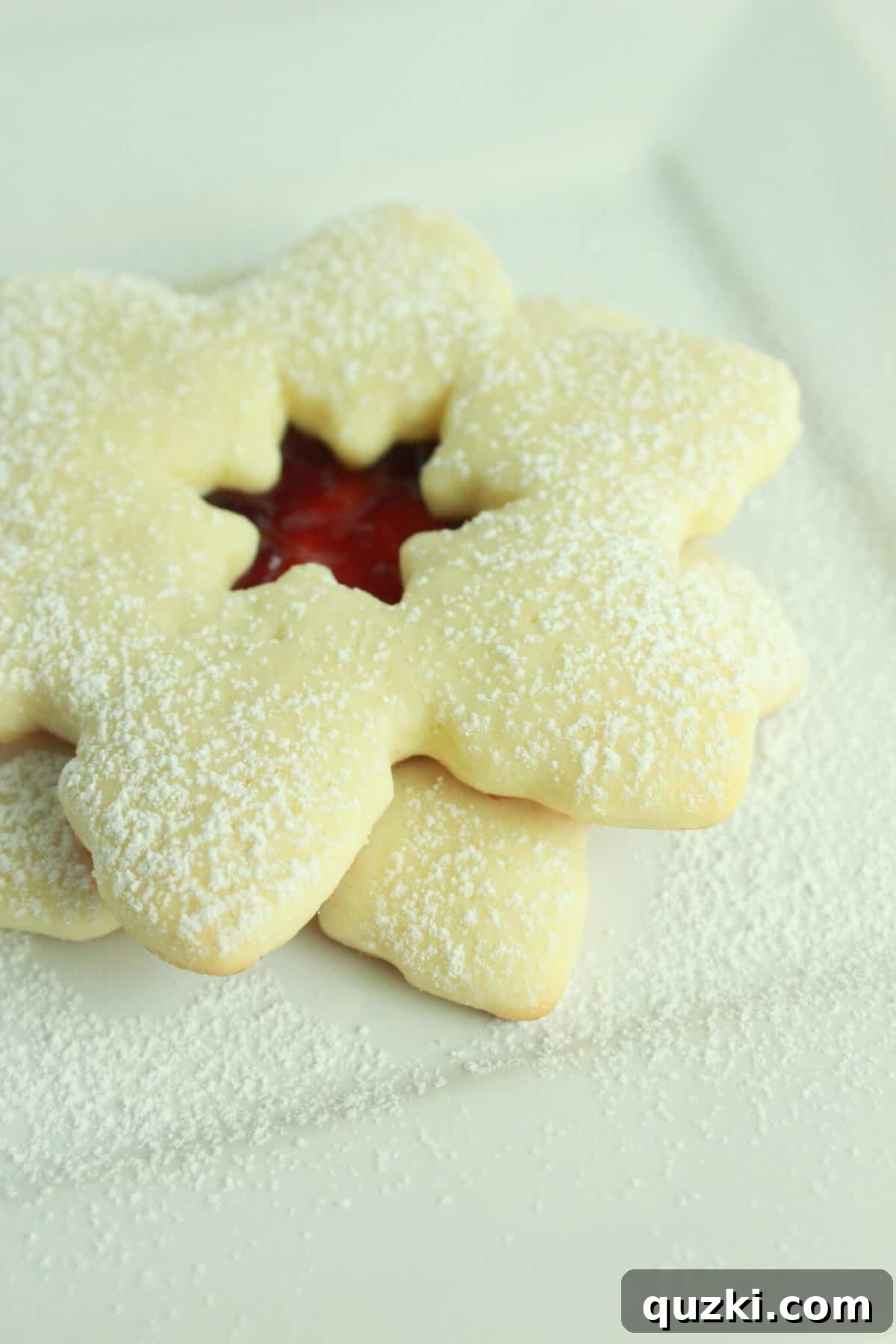 Beautiful snowflake Linzer cookies made from sugar cookie dough, filled with jam and dusted with powdered sugar