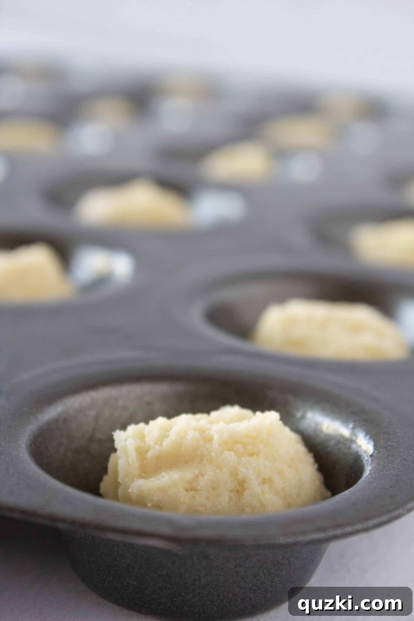 Adding small scoops of cake mix cookie dough into a mini muffin pan for Cannoli Cookie Cups.