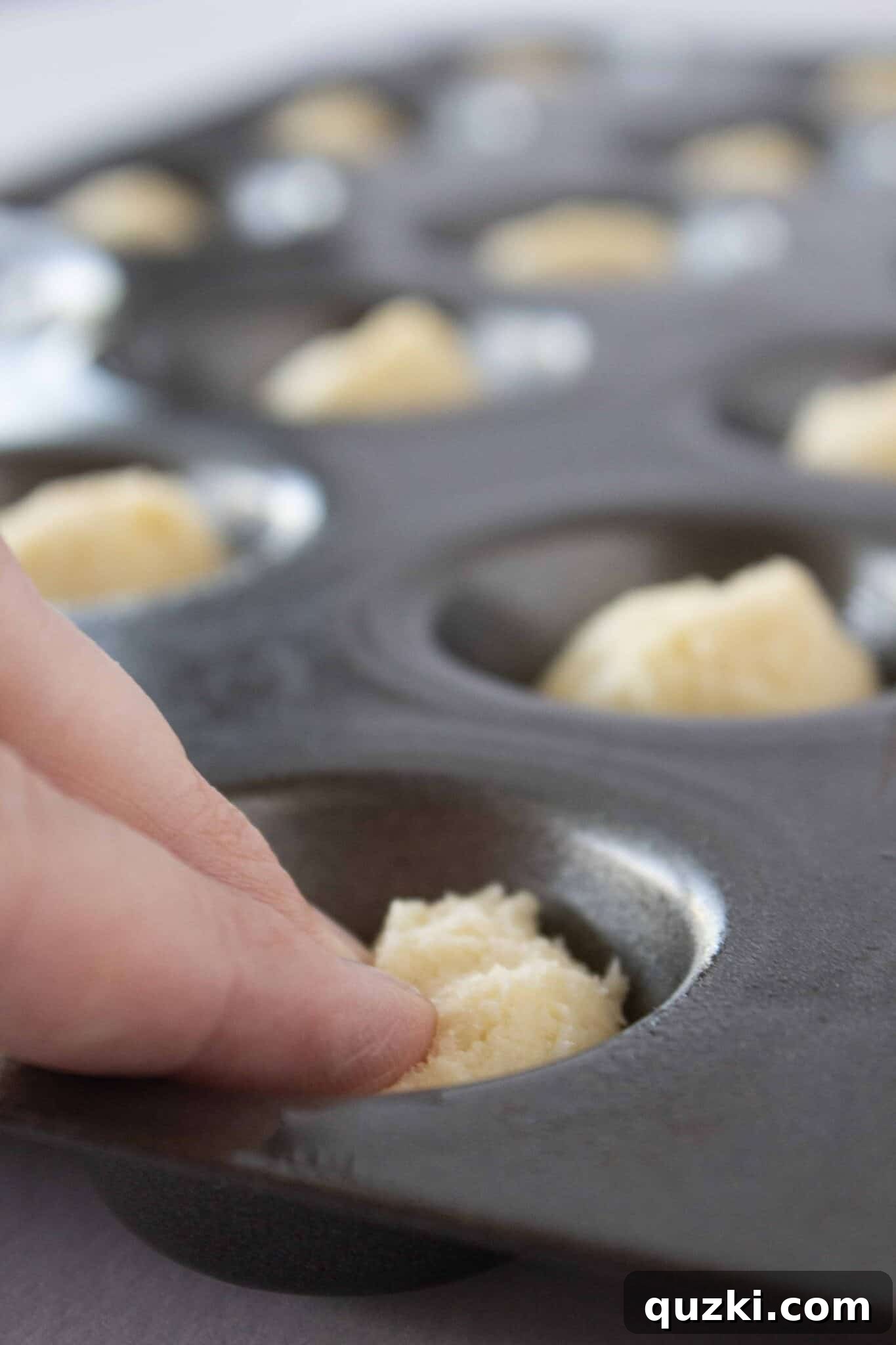 Using fingertips to gently press down the cookie dough in the muffin pan, creating a flat base for the cannoli cups.