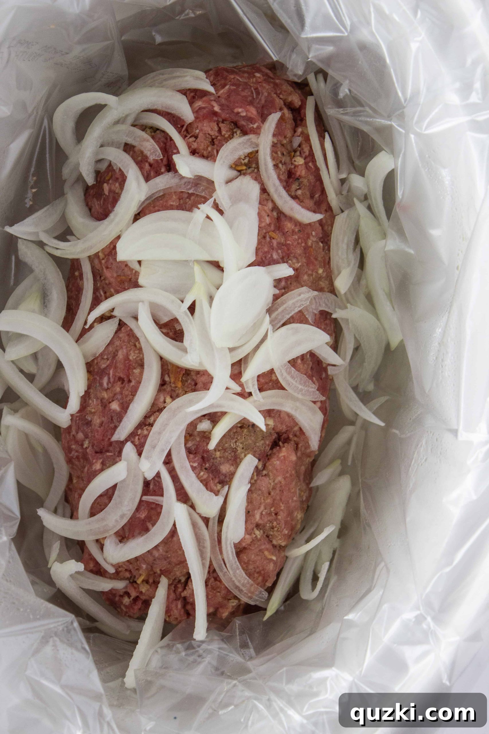 Adding onions and mushrooms to the top of the meatloaf in the crock pot.