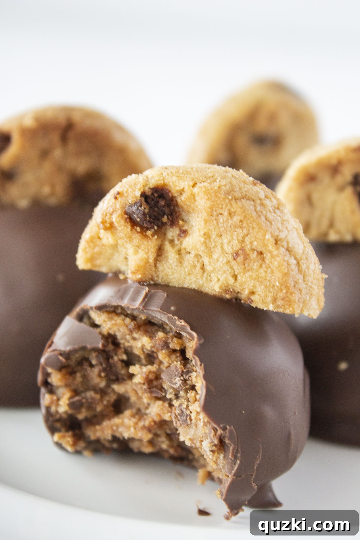 A tray of 4 chocolate chip cookie truffles with a bite taken out of the front truffle, showing the cookie crumb filling.