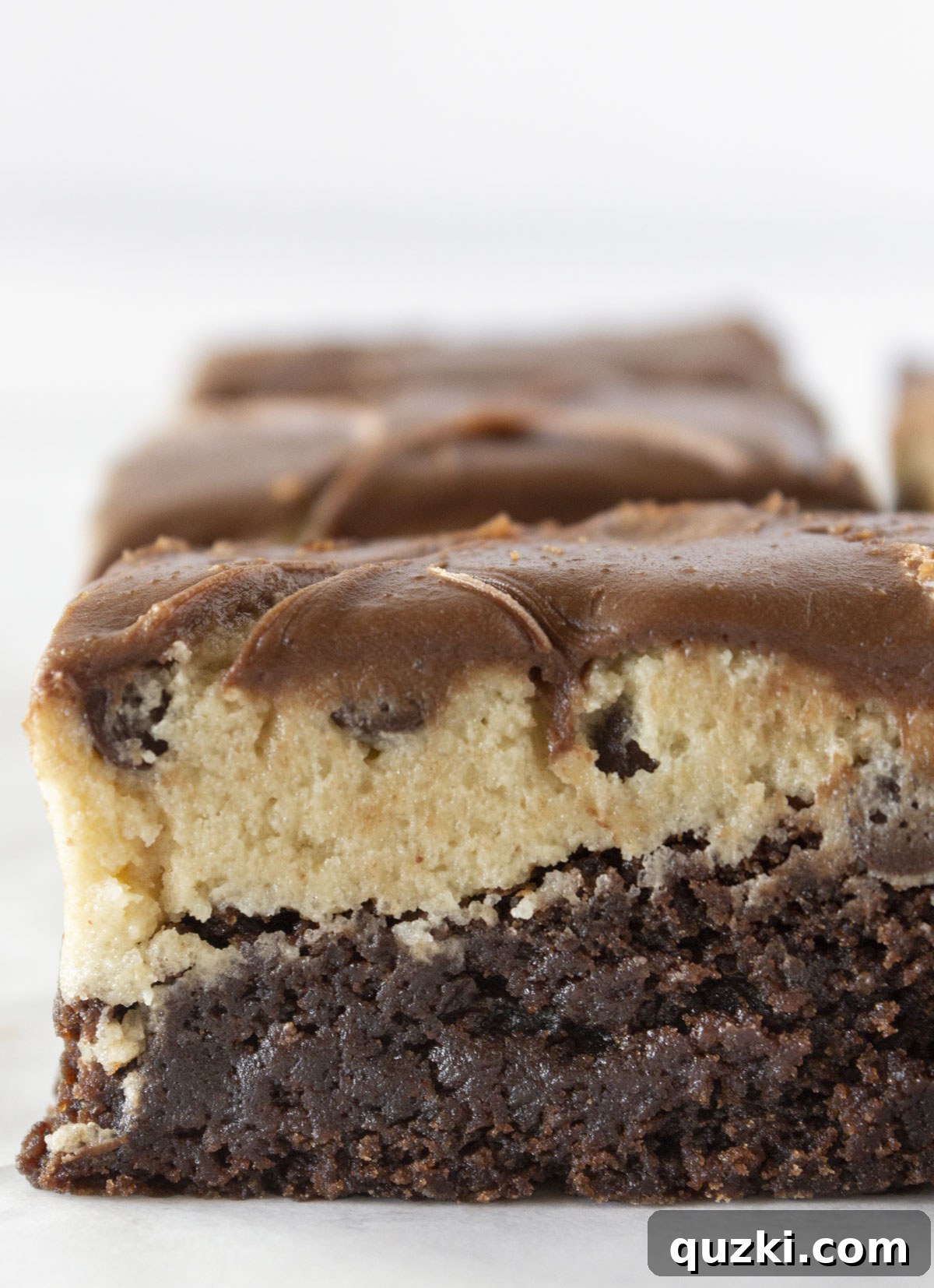 Cookie dough brownies in a line with one of them close up and being able to see all of the layers.