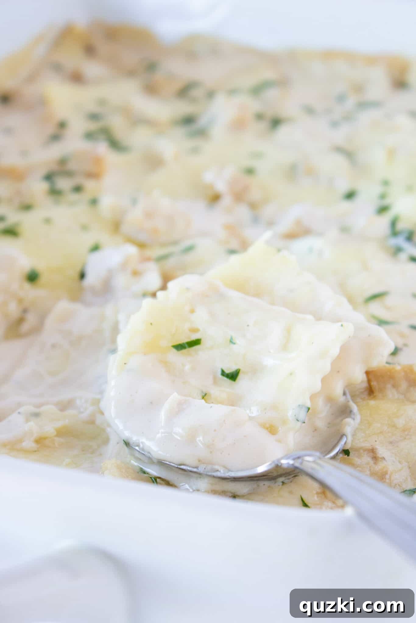 Creamy Chicken Alfredo Ravioli Bake 3 A spoon serving a generous portion of Alfredo chicken casserole, showcasing its creamy texture and rich ingredients.