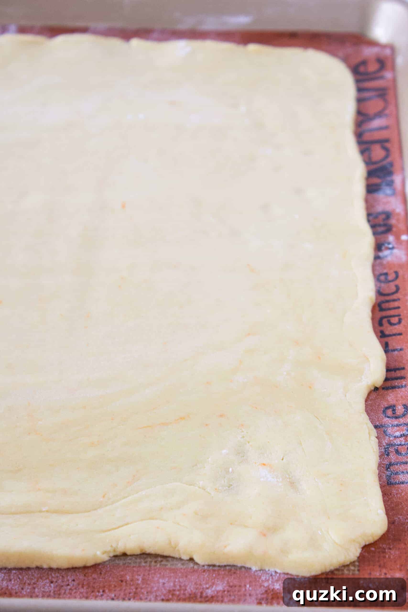 Cinnamon roll cookie dough rolled out onto a silicone mat, ready for filling