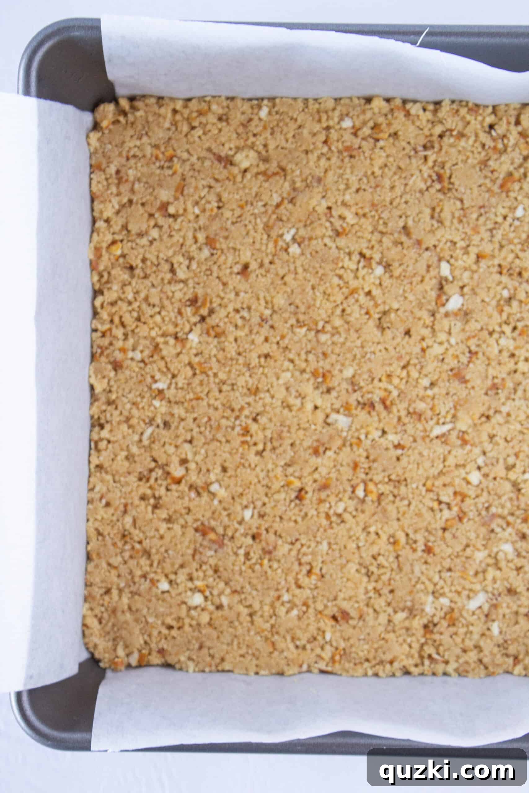 Pressing the shortbread and pretzel crust into a parchment-lined baking pan