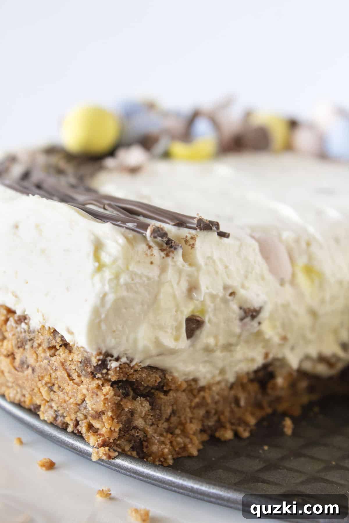 A close-up view of a sliced No-Bake Cadbury Mini Egg Cheesecake, revealing the creamy filling speckled with crushed mini eggs and the golden cookie crust.