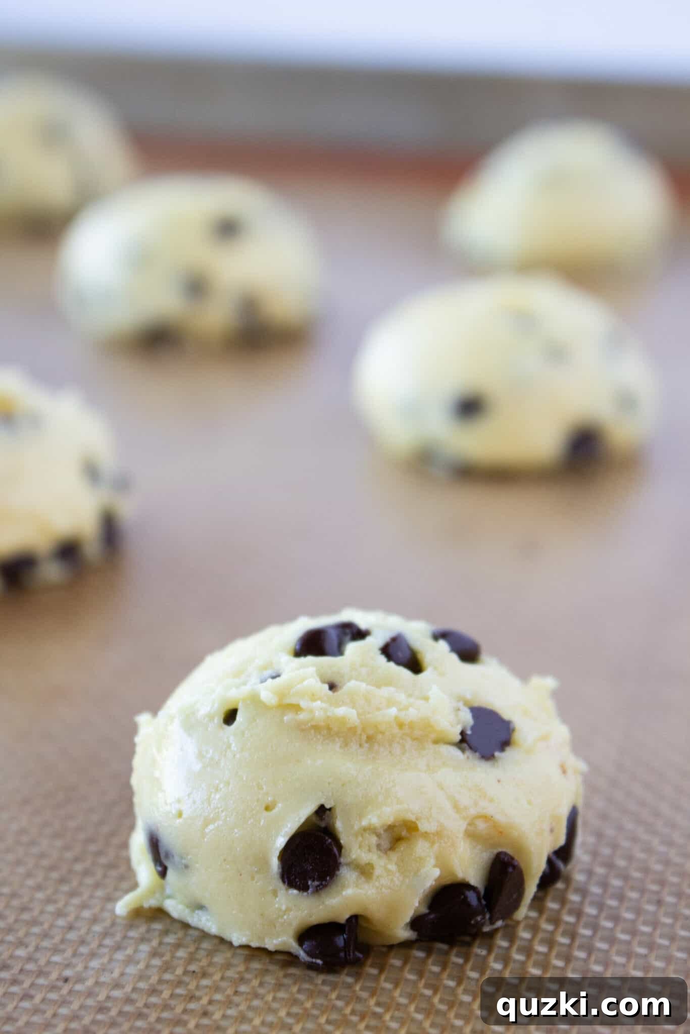 Uniformly scooped Chocolate Chip Sheet Cake Cookie dough placed on a parchment-lined baking sheet.